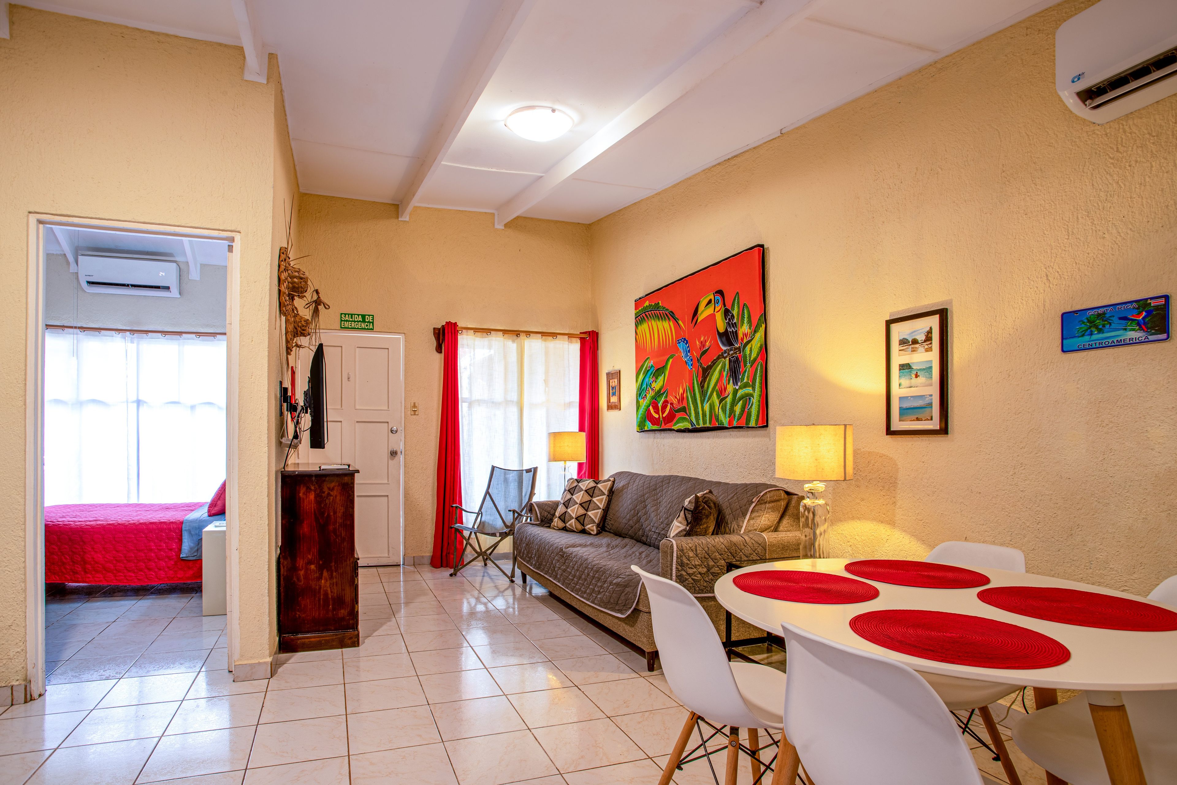 A hotel room with a bed, a sofa, a dining table with chairs, a lamp, and a painting on the wall.