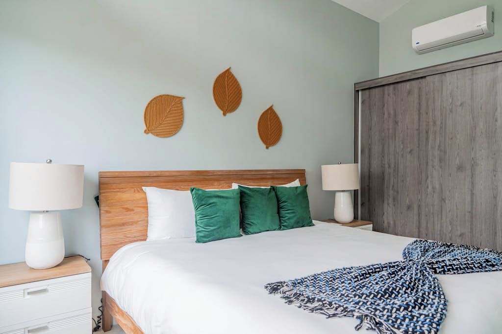 Una cama bien hecha con edredón blanco, almohadas verdes y una manta estampada en azul y blanco.