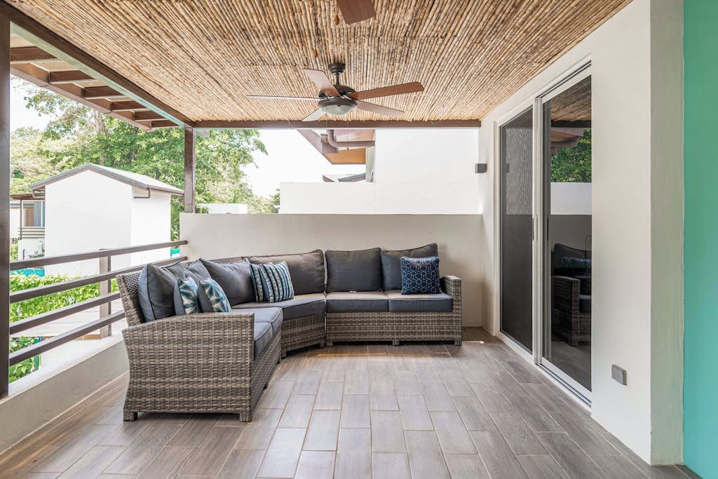 Een overdekt balkon met een wicker loungeset, een plafondventilator en een schuifdeur met glas.