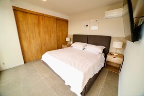 A bedroom with a large bed, wooden wardrobe, two bedside tables with lamps, and a flat-screen TV mounted on the wall. - Corazón de Zapopan - Cultura y gastronomía (Zapopan)