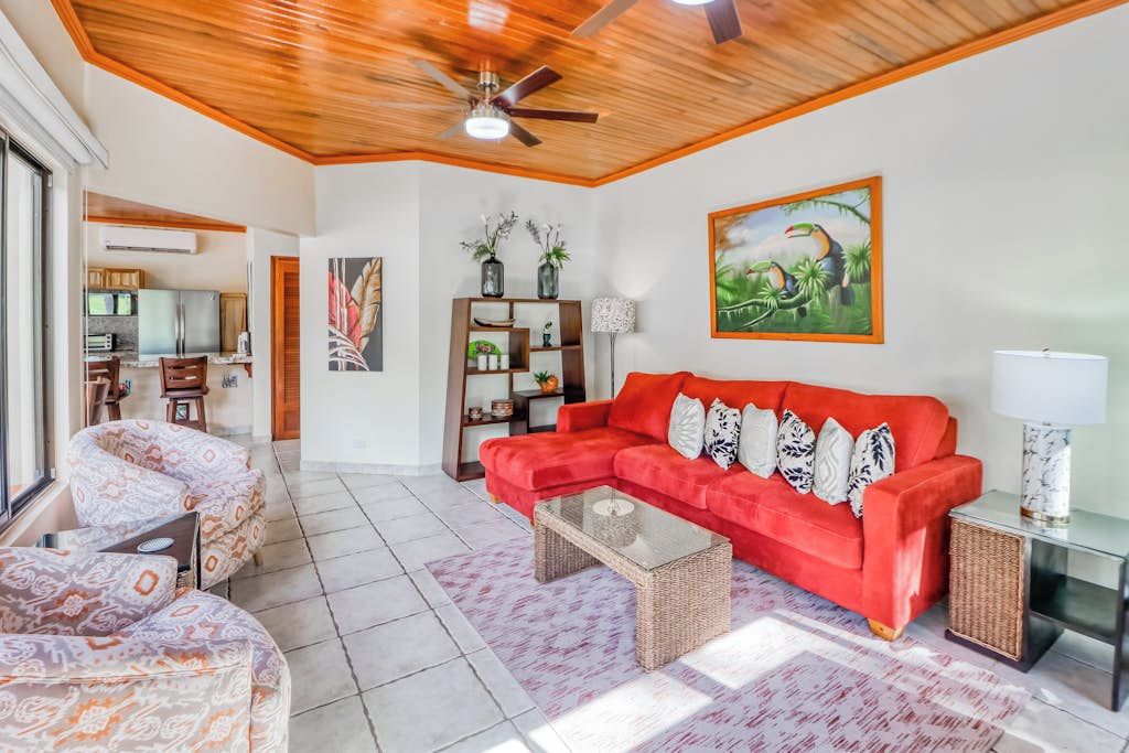 Una sala de estar con un sofá rojo, sillones estampados, una mesa de centro y un ventilador de techo.