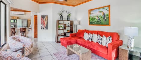 Una sala de estar con un sofá rojo, sillones estampados, una mesa de centro y un ventilador de techo.