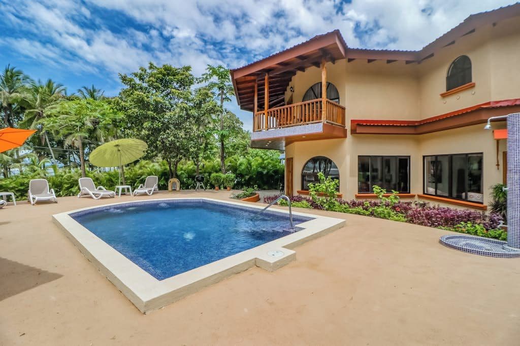 A pool area with lounge chairs and a two-story building with balconies.