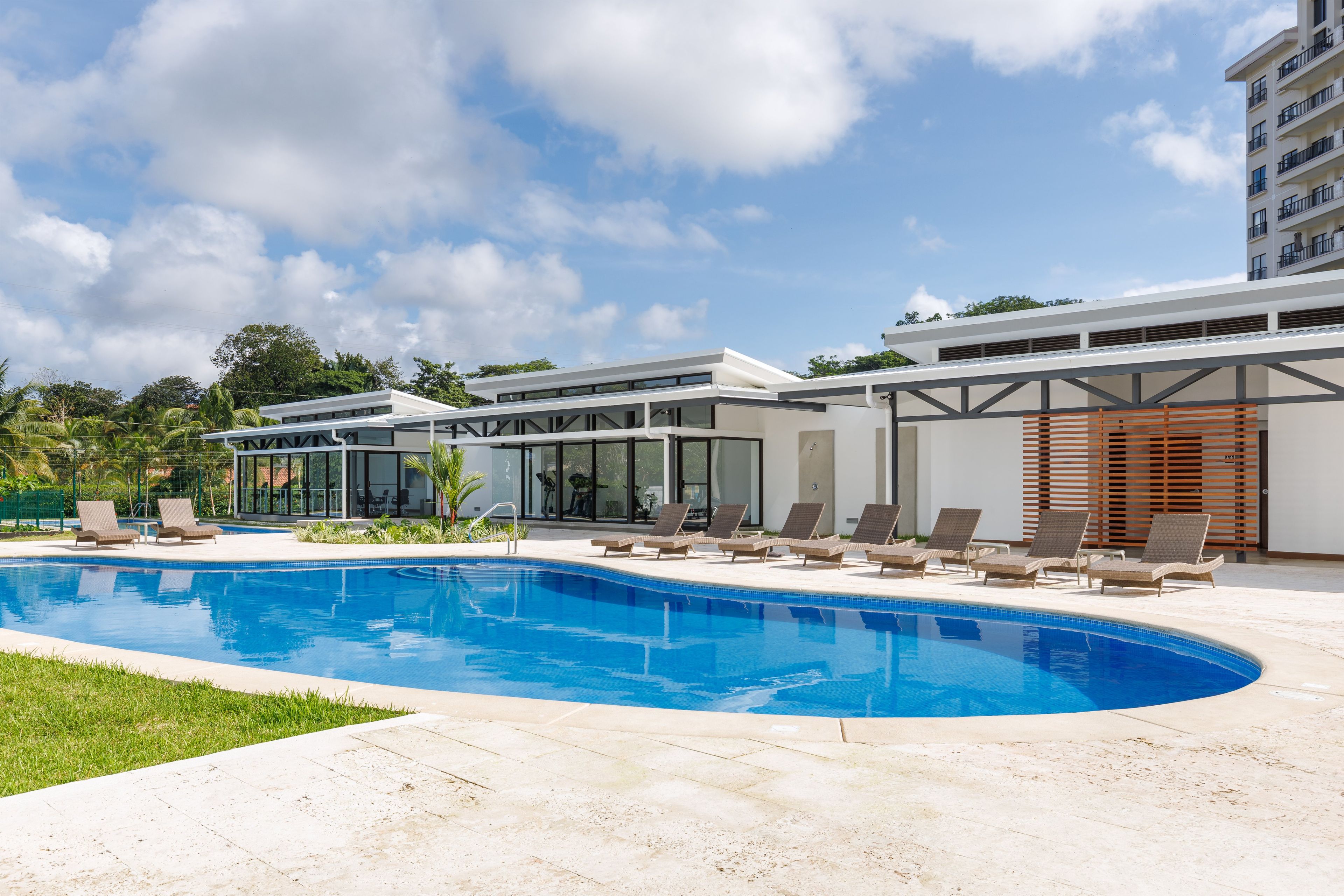 Un espace piscine moderne, doté de chaises longues et d’une piscine à l’eau cristalline, entouré d’un bâtiment aux grandes fenêtres et au toit plat.