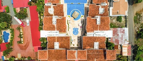 An aerial view of a hotel with multiple buildings, a central swimming pool, and surrounding greenery.