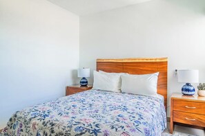 Ein Schlafzimmer mit einem hölzernen Kopfteil, einer blumigen Tagesdecke, zwei Nachttischen mit Lampen und einer kleinen Pflanze auf einem Tisch.