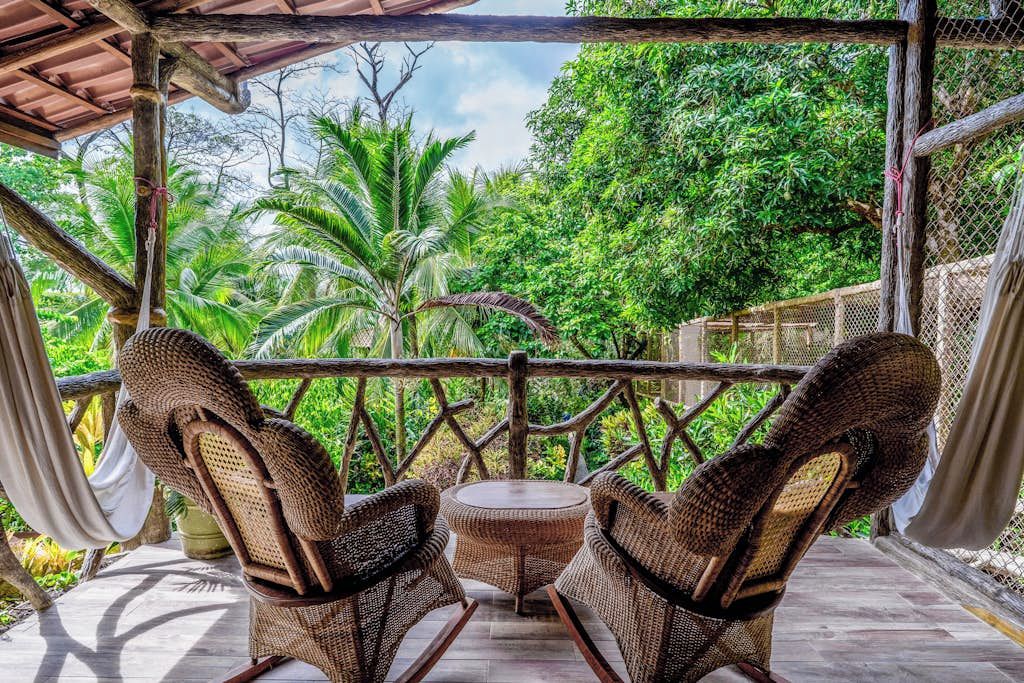 A covered outdoor seating area with wicker furniture and a view of lush greenery.