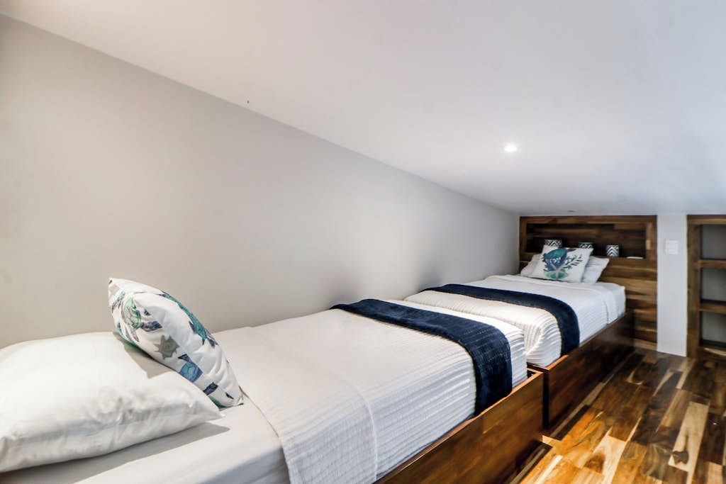 Una cama individual con cabecera de madera, ropa de cama blanca y una manta azul.