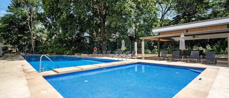 A rectangular swimming pool with a tiled edge, surrounded by lounge chairs and a covered seating area.