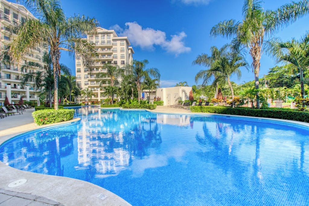 A swimming pool surrounded by palm trees and a multi-story hotel building.
