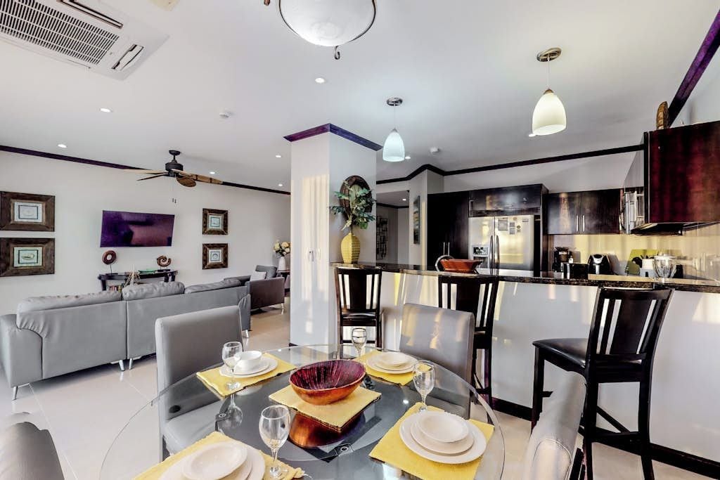 A modern dining area with a round table set for four, a kitchen in the background, and a ceiling fan.