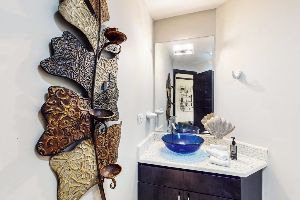 Ein Badezimmer mit einem Wanddekor, einem Waschbecken mit blauer Schüssel und einem dunklen Schrank.