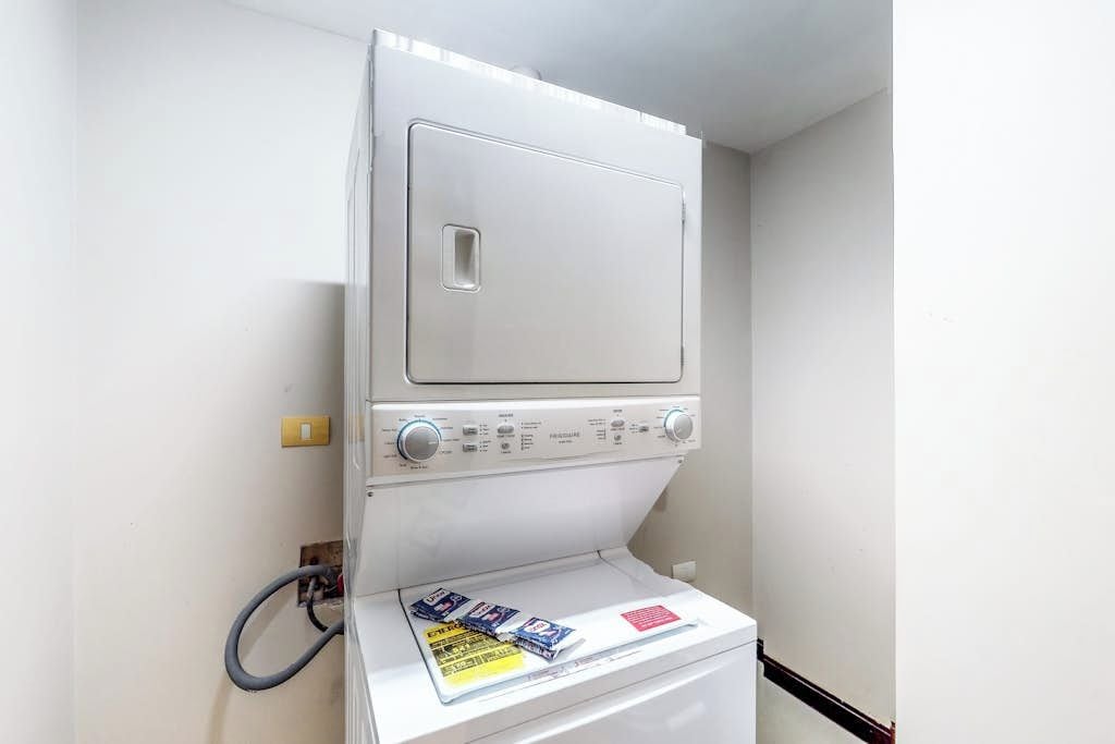 A stacked washer and dryer unit with control knobs and a hose.