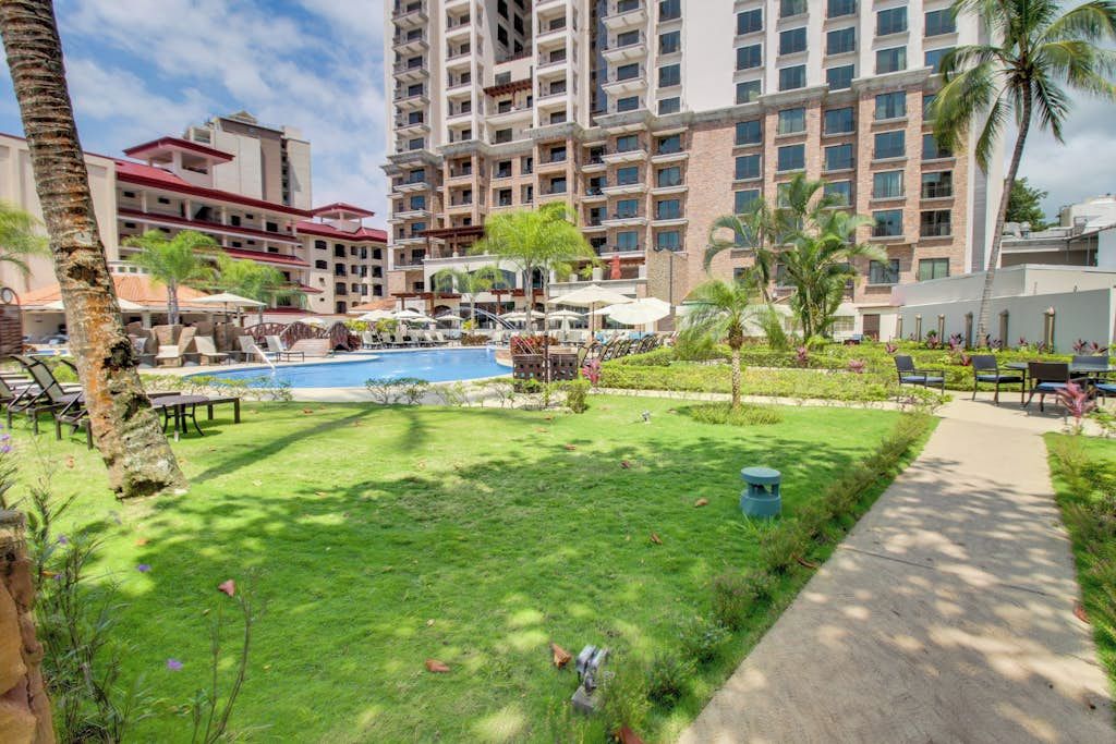A hotel courtyard with a swimming pool, lounge chairs, and palm trees.