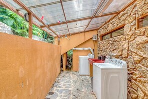 A laundry area with a washing machine and dryer, a stone wall, and a glass roof. - Casa Guarumo Monteverde Mountain View Retreat (Monteverde)