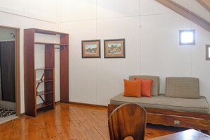 A room with a wooden floor, a sofa with cushions, a wooden cabinet, and two framed pictures on the wall. - Casa Guarumo Monteverde Mountain View Retreat (Monteverde)
