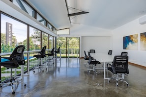 A modern conference room with large windows, black office chairs, and a white table. - Viva Jaco 1605 Modern Mountain View Apartment (Jacó)