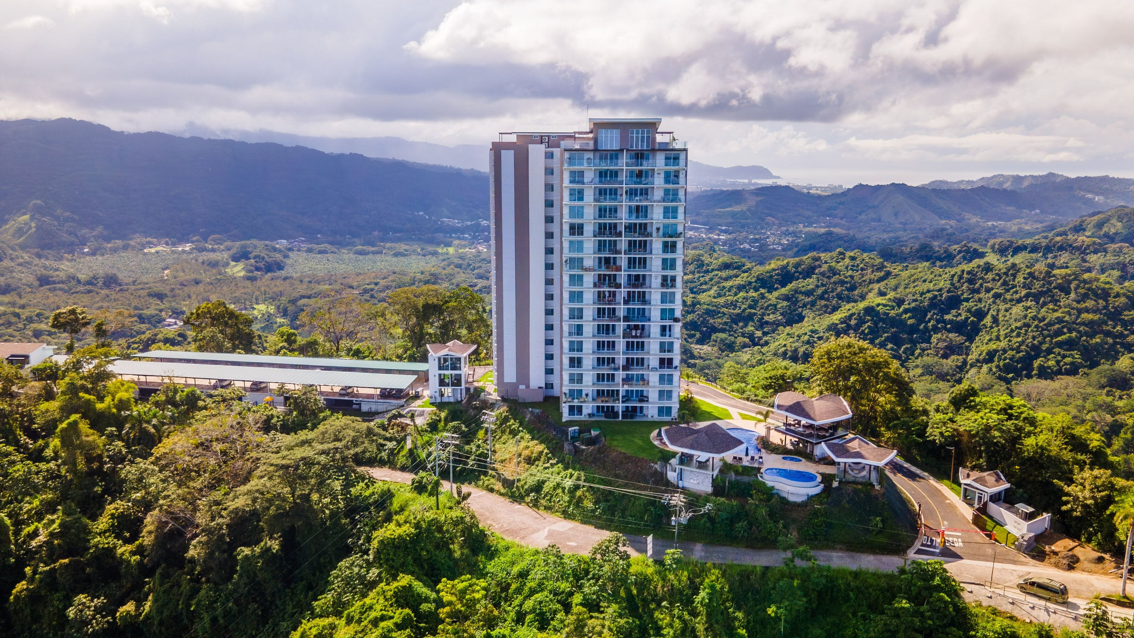 A high-rise hotel with multiple floors, surrounded by lush greenery and mountains in the background.