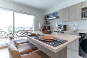 A modern kitchen with a central island, bar stools, and a dining area with a view. - Viva Jaco Ocean View 3BD/2BT (07-02C) (Jacó)