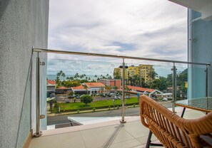 A balcony with a view of a parking lot, buildings, and palm trees. - Viva Jaco Ocean View 3BD/2BT (07-02C) (Jacó)