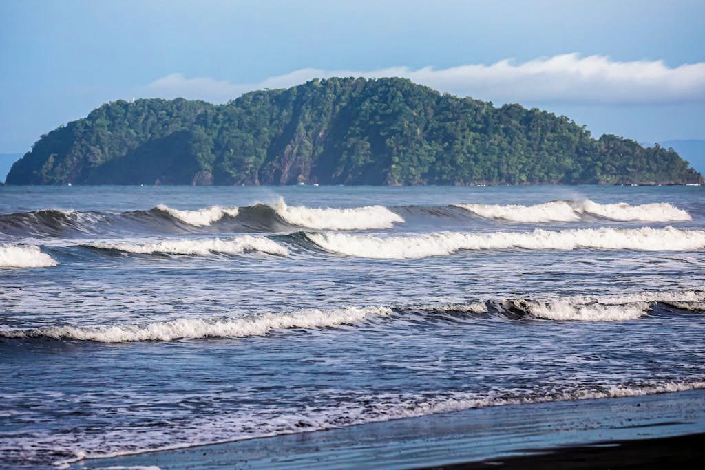A beach with waves and a forested island in the background.