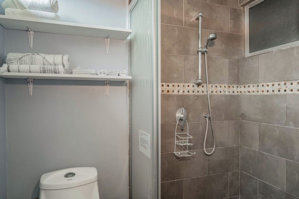 A bathroom with a shower, toilet, and shelves with towels.