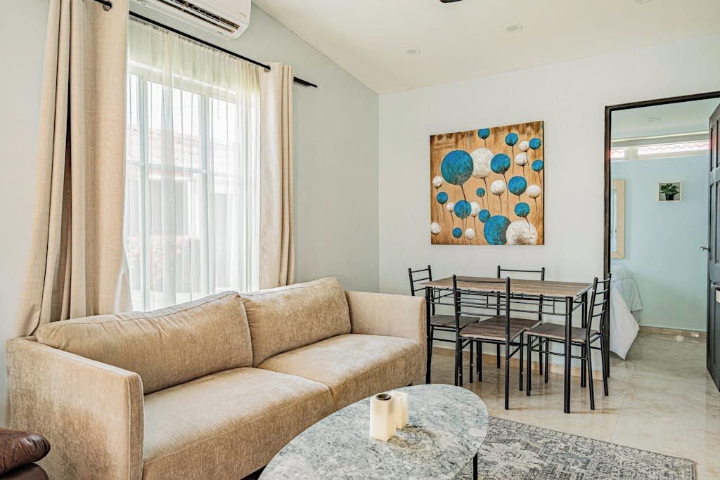 A living room with a beige sofa, a dining table with chairs, a marble coffee table, and a painting on the wall.