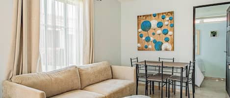 A living room with a beige sofa, a dining table with chairs, a marble coffee table, and a painting on the wall.