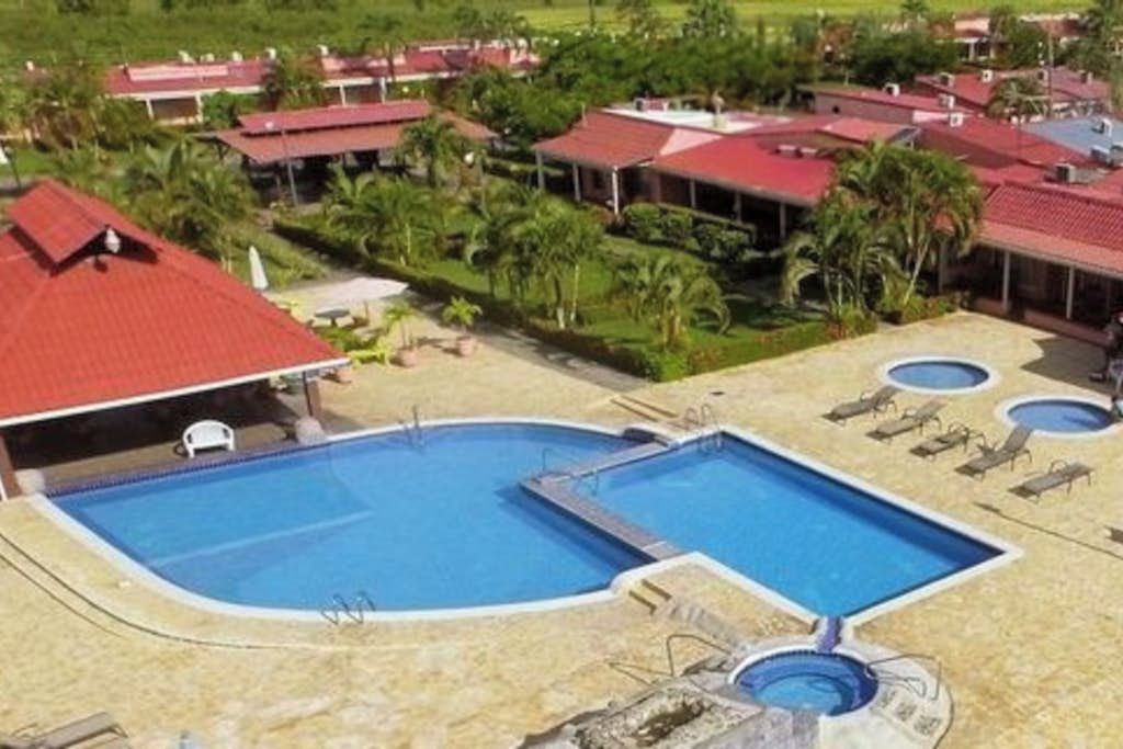 Un complexe hôtelier doté d’une grande piscine centrale, de plusieurs piscines plus petites et de nombreux bâtiments aux toits rouges.