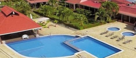 A resort with a large central pool, smaller pools, and multiple buildings with red roofs.
