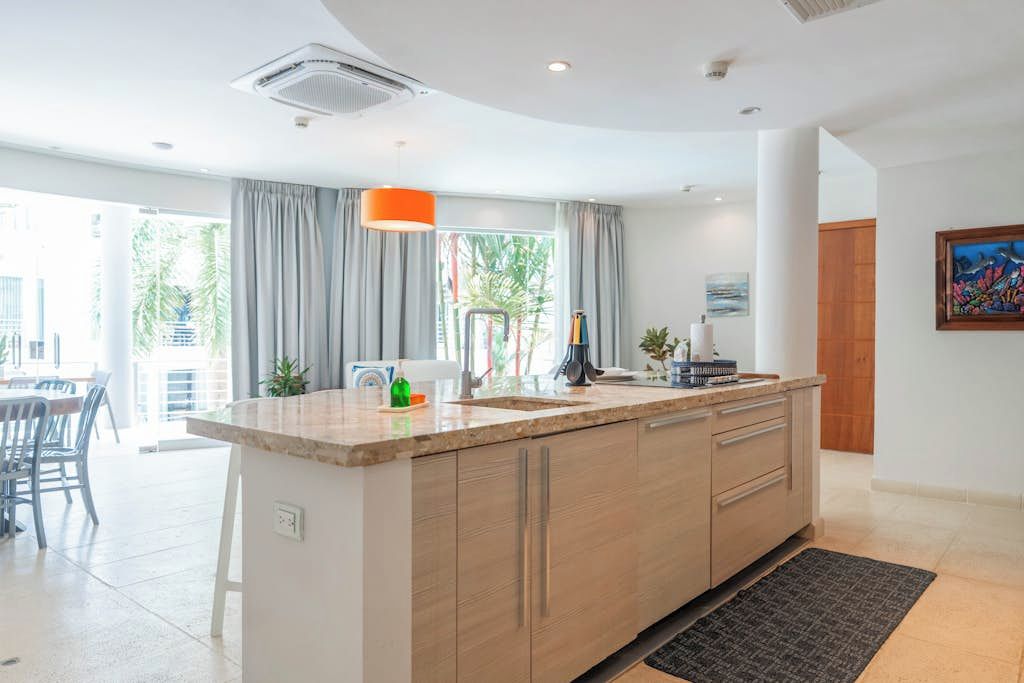 A modern kitchen with a central island, a dining area with chairs, and a view of the outdoors.