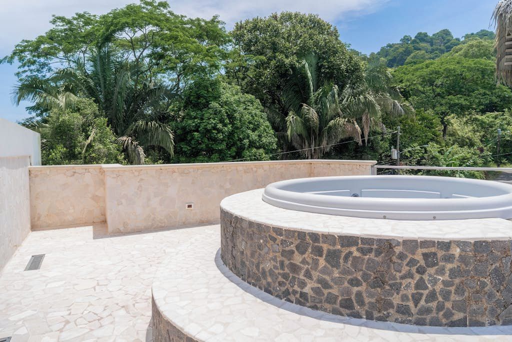 A circular stone structure with a pool, surrounded by a stone wall and a view of dense greenery.