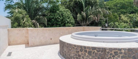 A circular stone structure with a pool, surrounded by a stone wall and a view of dense greenery.