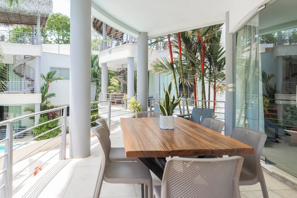 Un espace de restauration extérieur moderne, avec une table et des chaises en bois, entouré de murs en verre et donnant sur une piscine.
