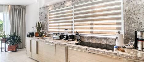 A modern kitchen with a marble countertop, built-in oven, and a large window with blinds.