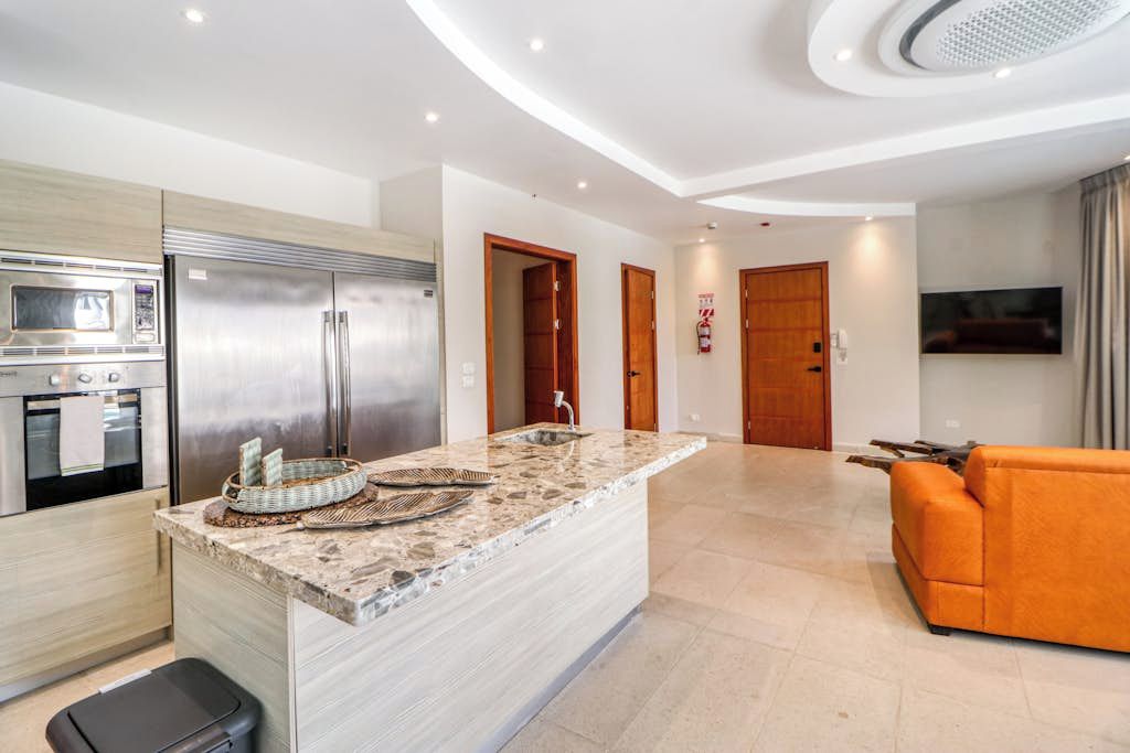 Een moderne keuken met een centraal eiland, roestvrijstalen apparatuur en een helder plafond.