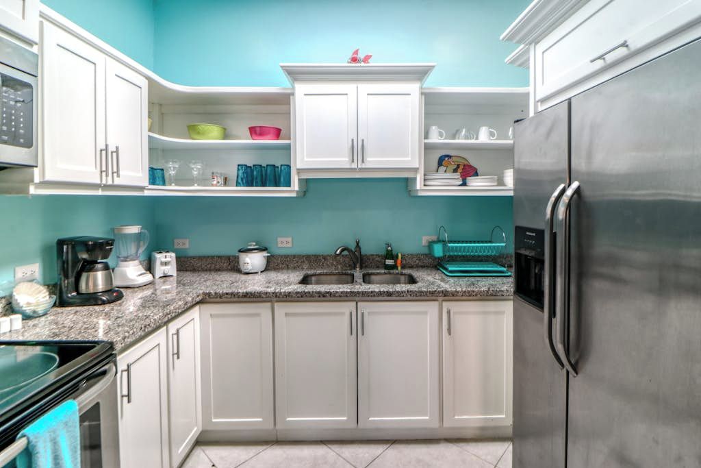 A kitchen with white cabinets, a stainless steel refrigerator, a granite countertop, and a teal backsplash.