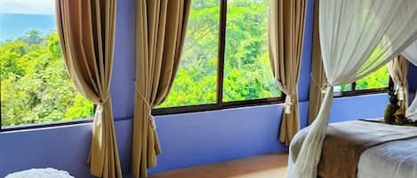 Ein Schlafzimmer mit großem Fenster, Vorhängen, einem Bett und einem kleinen runden Hocker.