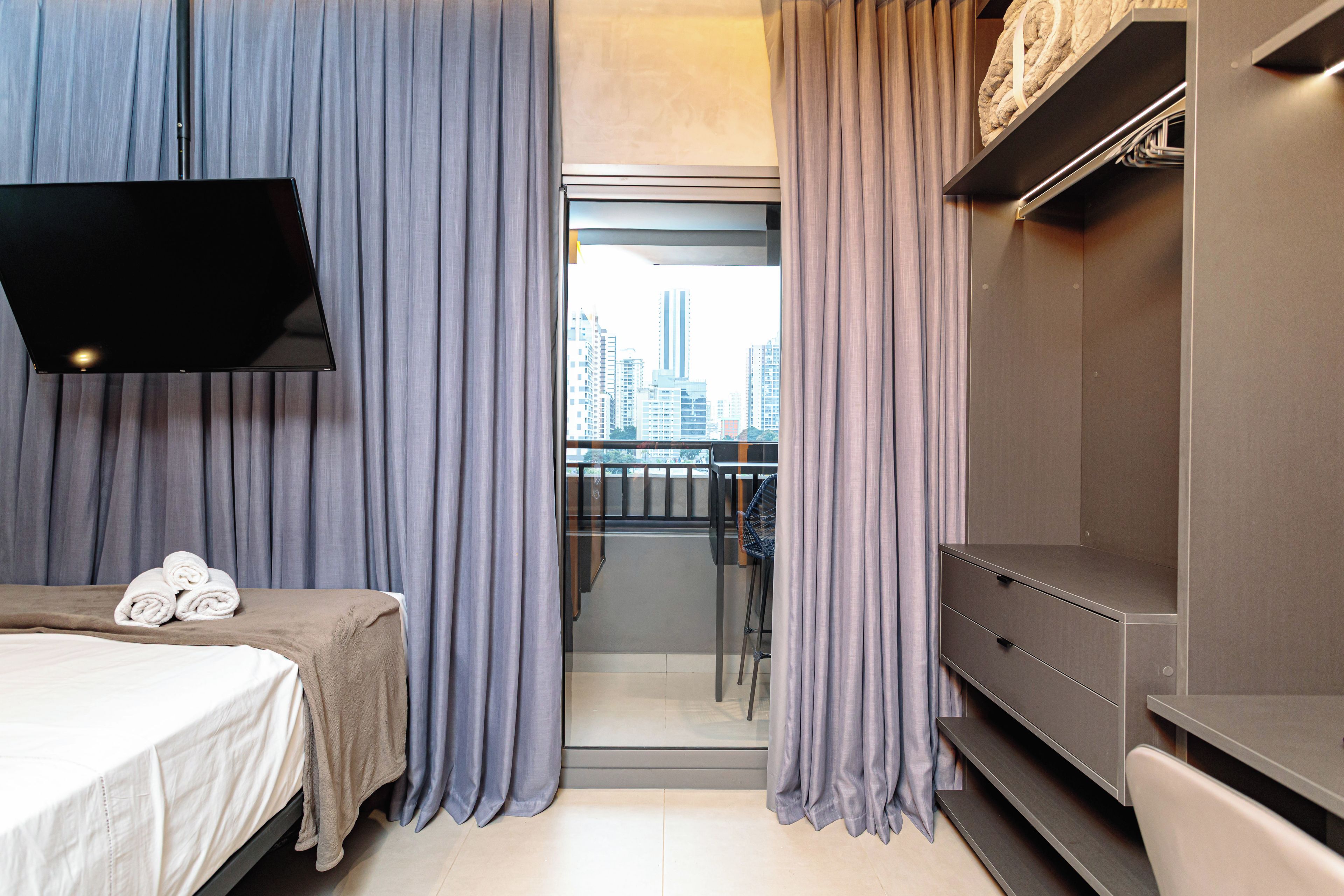 A hotel room with a bed, a flat-screen TV, a balcony with a city view, and a modern design.
