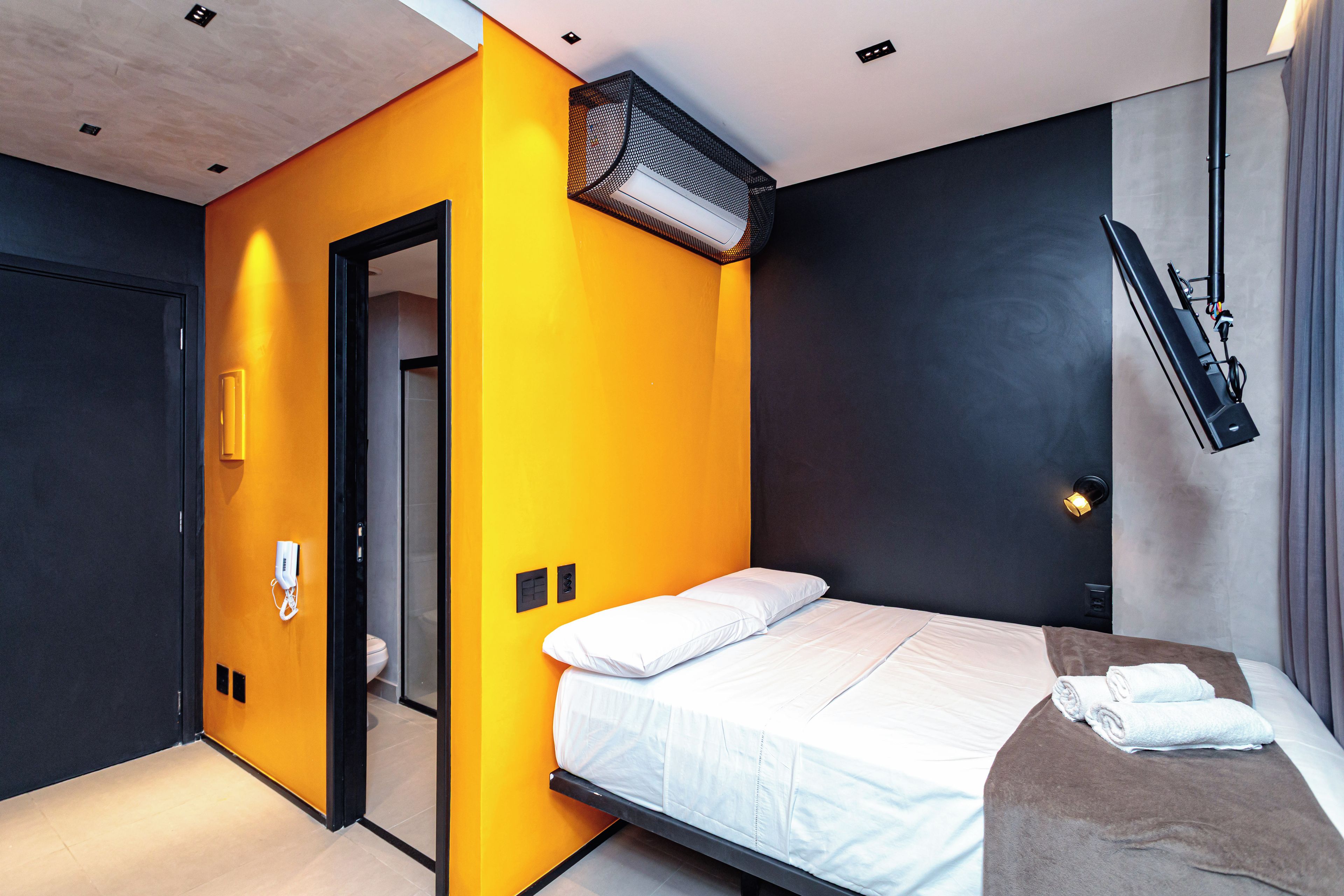 A modern hotel room with a bed, a bathroom, and a small seating area.