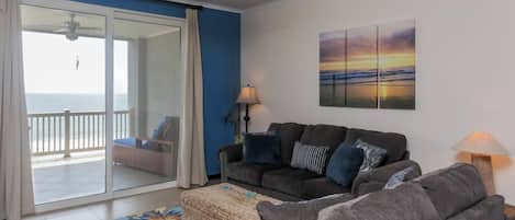 Een woonkamer met een bank, een salontafel en uitzicht op de oceaan door een schuifdeur.
