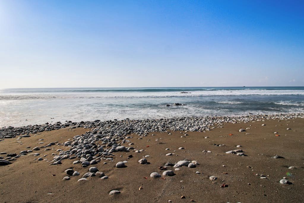 Een strand met een rotsachtige kustlijn en rustige golven.