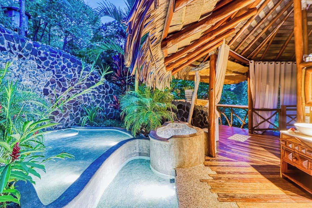 A spa area with a stone wall, a curved pool, and a wooden deck.