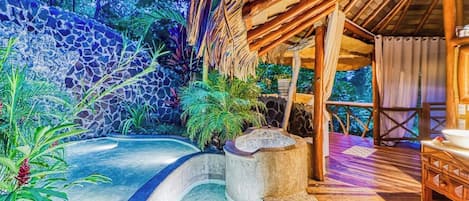 A spa area with a stone wall, a curved pool, and a wooden deck.
