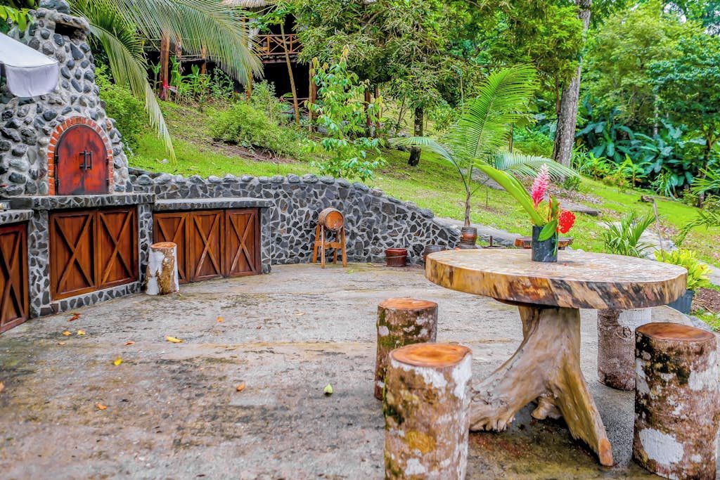 A stone-walled outdoor area with a round table and wooden stools.