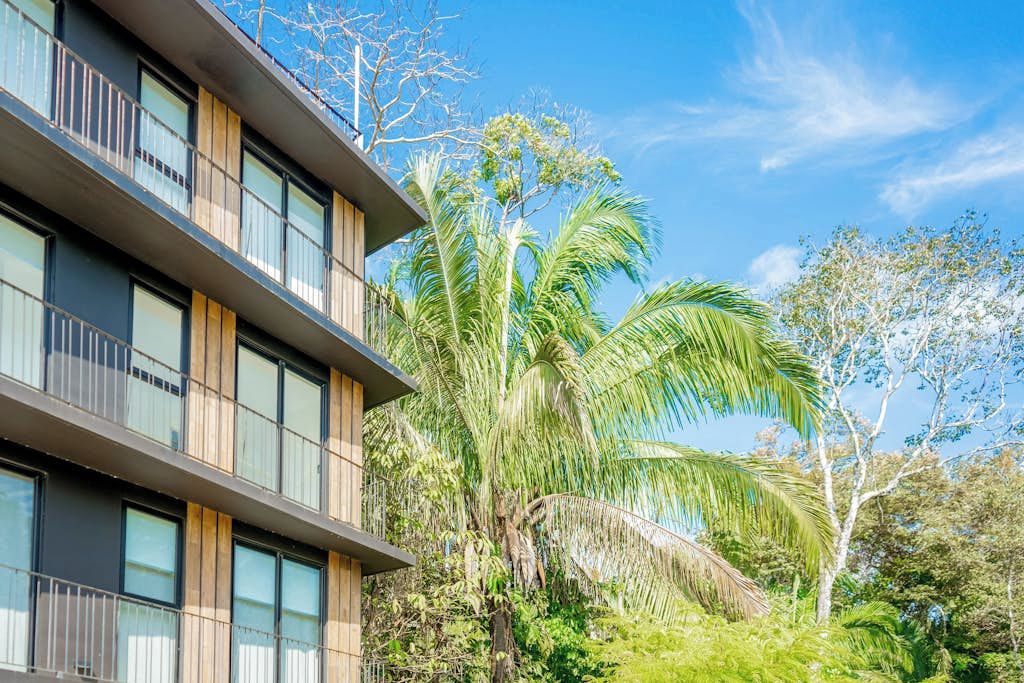 Een modern gebouw met meerdere balkons, omgeven door weelderige beplanting en palmbomen.