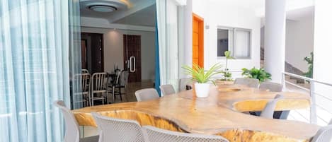A modern dining area with a large wooden table and white chairs, a potted plant, and a view of the interior space.
