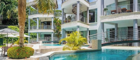 A multi-level hotel with a swimming pool, outdoor seating, and palm trees.