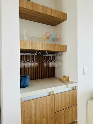 Eine Küche mit Holzausstattung, einer Arbeitsplatte und einem Weinkühlschrank mit Gläsern.