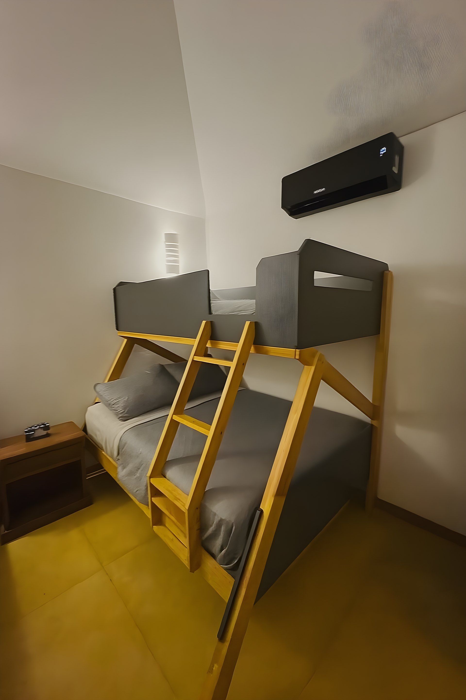 A bunk bed with a ladder, a bedside table, and a wall-mounted air conditioner.